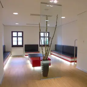 Modernes Wartezimmer mit Holzfußboden, roten Sitzbänken und dekorativer Baumvase.