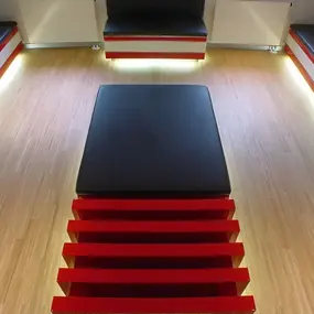 Modernes Wartezimmer mit schwarzen Sitzbänken, rotem Tisch und hellem Holzfußboden.