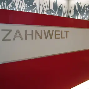 Moderne Zahnarztpraxis mit rotem Empfangstresen und dekorativem Grasmotiv an der Wand.