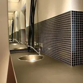 Modernes Badezimmer mit schwarzer Mosaikfliese, rundem Waschbecken und Spiegel.