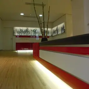 Modernes Zahnarztpraxis-Wartezimmer mit rotem Tresen, Holzfußboden und Pflanzen-Dekor.