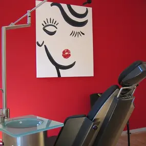 Moderner Kosmetikstudio-Raum mit roter Wand, Behandlungsstuhl und stilvollem Wandbild.